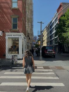 a woman walking across a cross walk in front of a store