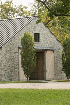 an old stone building with a metal roof and door in the middle of a grassy area