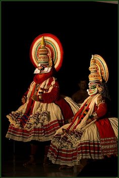 two people dressed in costumes and headgear performing an artistic dance on the stage