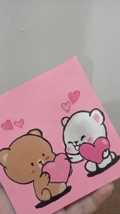 a hand holding up a pink card with two teddy bears and heart shapes on it