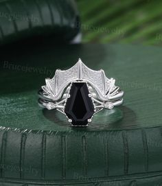 a black diamond ring sitting on top of a green leafy tablecloth with leaves around it