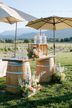 an outdoor bar with umbrellas and flowers on the grass in front of some wine barrels