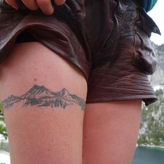 a woman with a tattoo on her thigh showing the mountain range behind her back leg