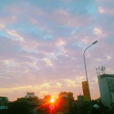 the sun is setting over some buildings and people are walking down the street in front of it