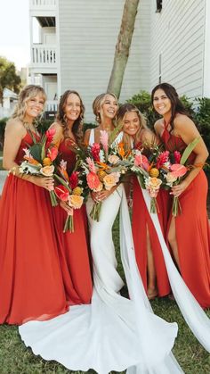 a group of women standing next to each other in front of a house holding bouquets