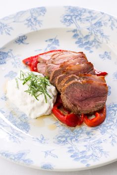 a white plate topped with meat and veggies on top of a blue flowered plate