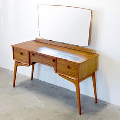 a wooden desk with a mirror on top of it next to a wall in an empty room