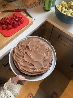 a person holding a cake with chocolate frosting on it and strawberries in the background