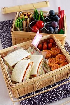 two wicker baskets filled with sandwiches and fruit on top of a white table cloth