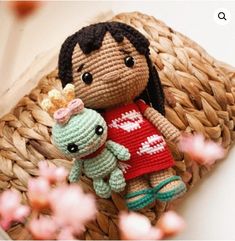 a small crocheted doll holding a stuffed animal in her arms on a wicker basket