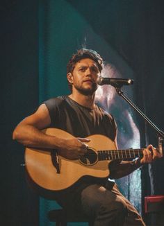 a man sitting in front of a microphone while holding a guitar and singing into a microphone