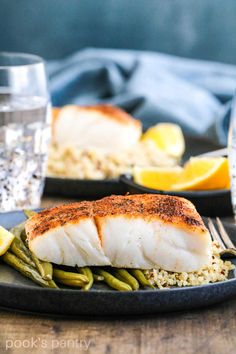 two black plates with fish and green beans on them, next to glasses of water