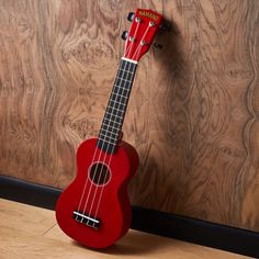 a red ukulele sitting on top of a wooden floor next to a wall