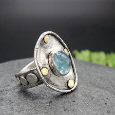 "A beautiful and very interesting Aquamarine, silver and gold ring. Minimalistic elegance is the main attribute of this beautiful piece. The design recalls ancient times and cultures, and some pieces of its surface are oxidated and scratched to give a more textured feeling to it. The main protagonist, is a transparent, clear and intense Aquamarine. The main material of this beauty is the sterling silver, while the details around the gem are made of 18 kt gold. This piece is entirely made by myse Modern Handmade Moonstone Ring For Gift, Artisan Rings With Bezel Setting, Handmade Fusion Style Moonstone Ring As Gift, Handmade Fusion Style Moonstone Ring For Gift, Unique Blue Topaz Ring, Handmade Modern Moonstone Ring For Anniversary, Handmade Adjustable Topaz Ring For Anniversary, Unique Rings With Bezel Setting As Gift, Unique Rings With Bezel Setting For Gift