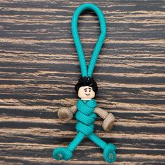 a keychain with a blue rope and a small doll on it's side