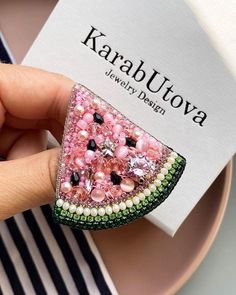 a person is holding a brooch with pink and green sequins on it