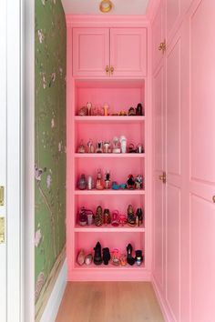 the closet is painted pink and has many pairs of shoes on shelves that are lined up against the wall