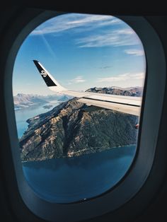 an airplane wing flying over a large body of water with mountains in the back ground