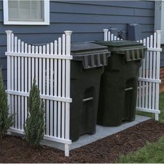 two trash cans sitting next to each other in front of a blue house with white picket fence