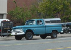 an old blue truck is parked on the side of the road next to a bus