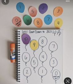 a spiral notebook with numbers and balloons on it, next to a marker board that says let's count down to twenty