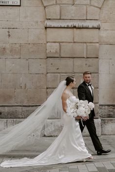 Bride in corset style wedding dress with long train holding white structural wedding bouquet with long veil with groom in black tuxedo for city wedding Corset Style Wedding Dress, Traditional Wedding Vows, Monochrome Weddings, City Wedding Venues, London Wedding Venues, Traditional Wedding Attire, Traditional Wedding Invitations, Long Veil, White Wedding Bouquets