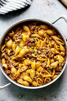 a large pot filled with pasta and meat on top of a gray counter next to a wooden spoon