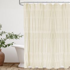 a white shower curtain in a bathroom next to a bathtub and potted plant