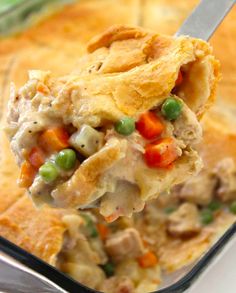 a spoonful of chicken pot pie with peas and carrots on it, in a casserole dish