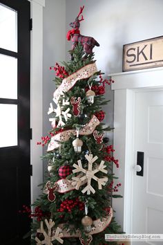 a christmas tree decorated with red and white ribbon, ornaments and deers on it