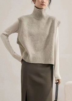 a woman standing with her hands on her hips wearing a turtle neck sweater and skirt