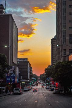 cars are driving down the street in front of tall buildings at sunset or sunrise time