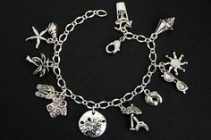 A collection of silver plated beach vacation themed charms have been dispersed around a shimmering silver plated bracelet chain in this handmade charm bracelet. This summer vacation charm bracelet is then completed with a lobster clasp and a 1/2 inch of chain at the end for adjustable sizing. Charms in this bracelet include a tropical drink charm, conch charm, sunglasses charm with sun charm, bare feet charm, beach chair with umbrella charm, sand dollar charm, tropical shirt charm with flipflops Beach Jewelry With Metal Charms, Beach Jewelry With Dangling Metal Charms, Beach Metal Bracelets With Charms, Beach Jewelry With Lobster Clasp, Metal Charm Bracelets For Beach, Beach Metal Jewelry With Starfish Charm, Silver Beachy Jewelry For Beach Occasions, Beachy Silver Beach Jewelry, Beach Charms Bracelet Jewelry