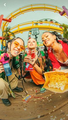 three women taking pictures with their cell phones while sitting on the ground at an amusement park