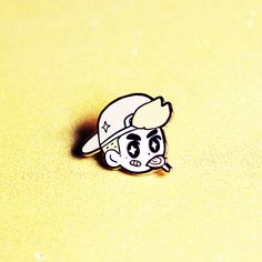 a pin with a cartoon character wearing a baseball cap on it's head, sitting on a yellow surface