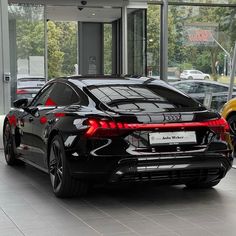 the rear end of a black sports car parked in front of a building with glass doors