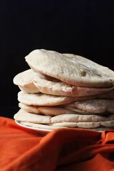 a stack of pita bread sitting on top of a white plate next to an orange cloth