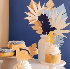 some cupcakes are sitting on a table next to a vase and paper cutouts