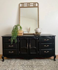 a black dresser with a mirror and potted plant on top in front of it