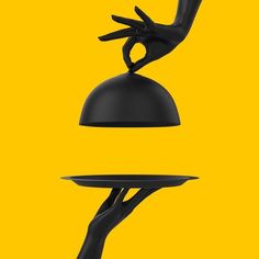 a hand reaching for a serving dish on top of a black cake platter, against a yellow background