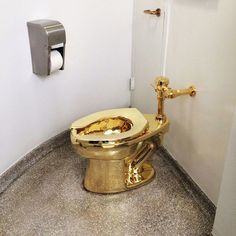 a gold toilet with the lid up in a bathroom stall, next to a roll of toilet paper