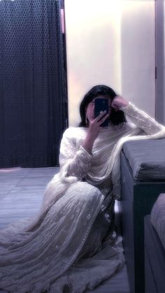 a woman in a white dress taking a selfie with her cell phone while sitting on a bed