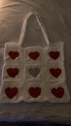 a white crocheted bag with red and gray hearts on it sitting on a bed