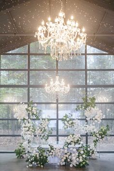 a chandelier hanging from the ceiling over a table with white flowers and greenery