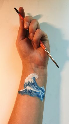 a hand holding a paintbrush with a wave painted on it's wrist and the tip of an artist's arm