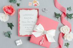 the wedding stationery is decorated with pink and white flowers, ribbons, and rings