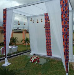 an outdoor wedding setup with white draping and red flowers on the grass in front of it