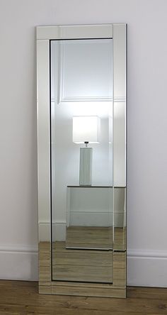 a large mirror sitting on top of a wooden floor next to a wall mounted lamp