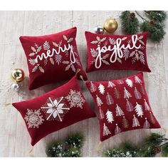 three red christmas pillows with white snowflakes and merry lettering on them sitting next to pine cones