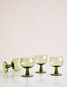 four green glass goblets sitting on top of a white table next to each other